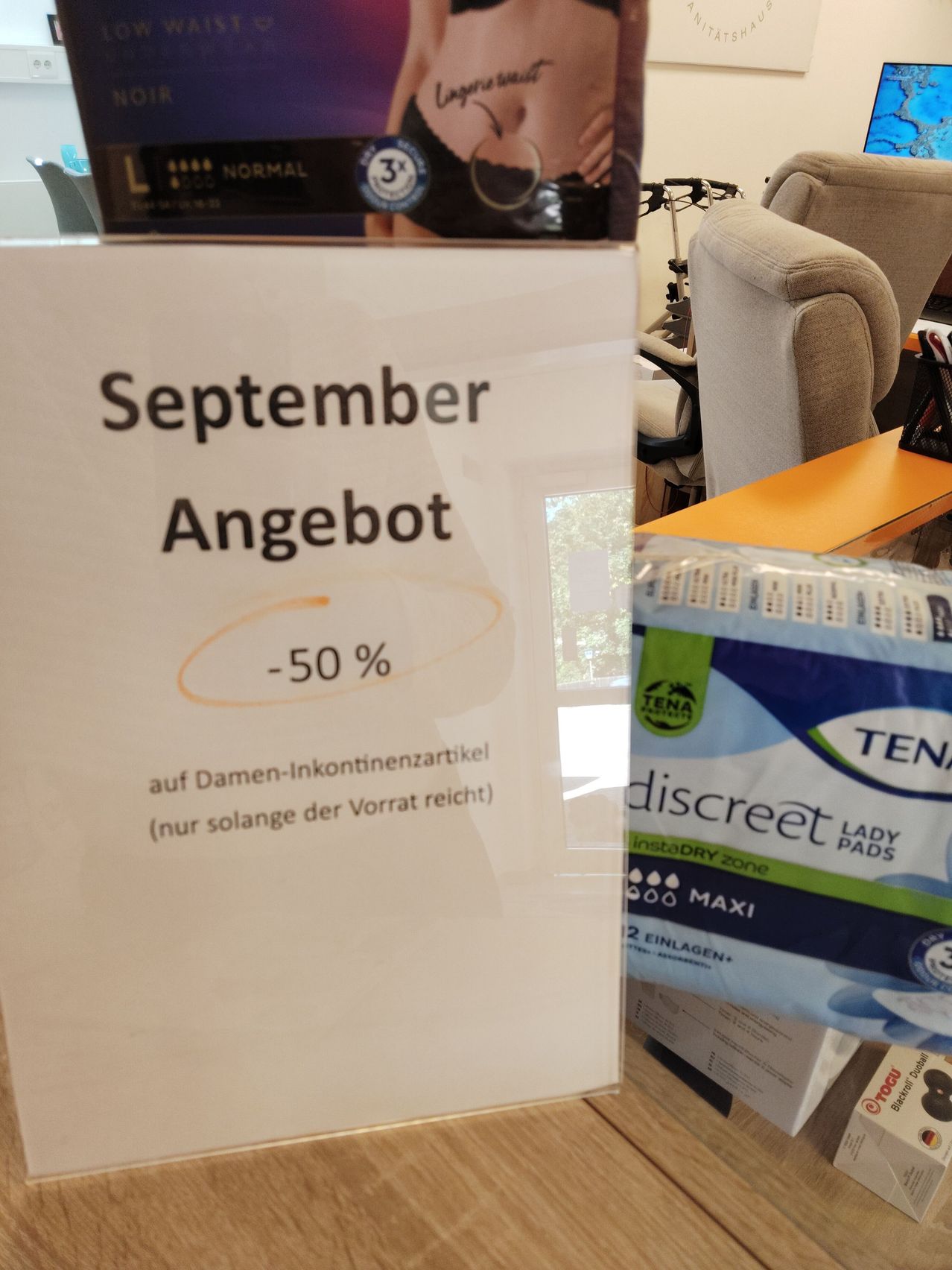 Ein Werbeschild für den September bietet 50% Rabatt auf Damen-Inkontinenzartikel. Das Schild befindet sich neben einer Packung TENA Discreet Lady Pads.