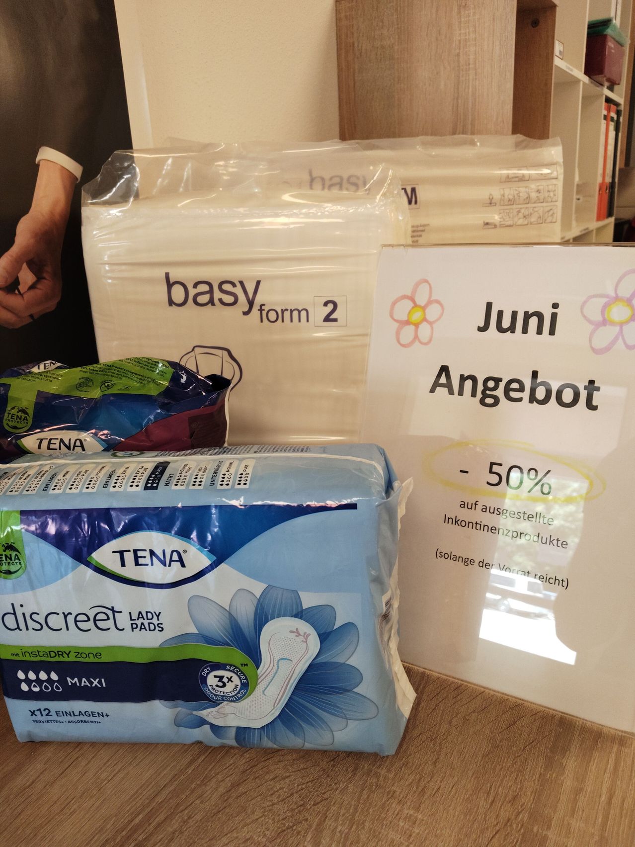 Eine Ausstellung von Tena Inkontinenz-Pads, einschließlich diskreter Maxi-Pads, in einem Geschäft mit einem Schild, das 50% Rabatt auf ausgestellte Inkontinenzprodukte anbietet.