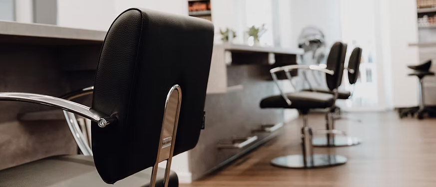 Ein Salon-Innenraum mit einem schwarzen Lederstuhl und einer Metallbasis. Dahinter befinden sich drei schwarze Salonstühle mit einer silbernen Basis.