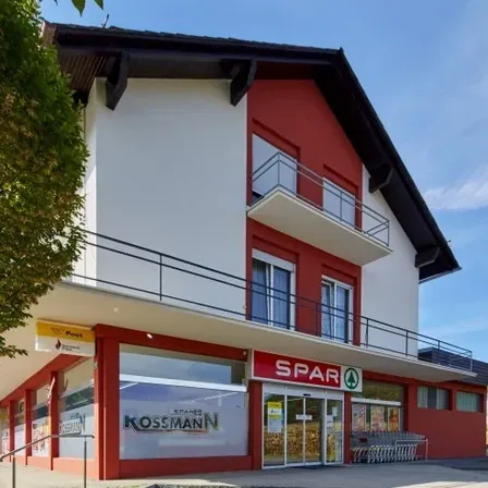 A red and white building with a balcony and a sign reading 'SPAR' is located in a rural area.
