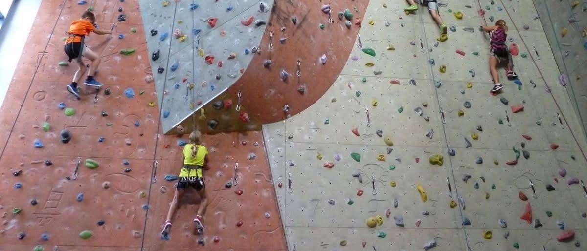 Zwei Kletterer in gelben Shirts klettern eine Felswand. Ein Kletterer ist in der Nähe der Spitze, während der andere in der Mitte der Wand ist.