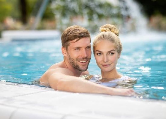 Ein Paar genießt einen romantischen Moment in einem Schwimmbad mit einer Fontäne im Hintergrund.