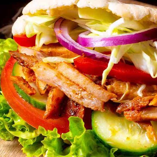 Nahaufnahme eines Hähnchen-Schawarma-Sandwichs mit Salat, Tomaten und Zwiebeln. Das Sandwich ist aufgeschnitten.
