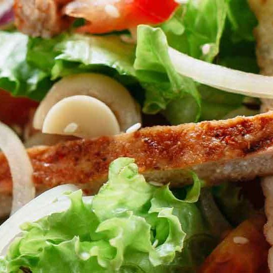 Nahaufnahme eines frischen Salats mit Hähnchen, Salat, Champignons und Zwiebeln auf einem Teller.
