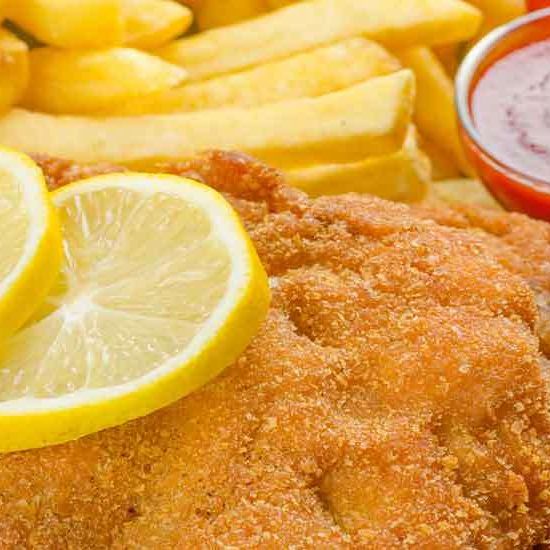 Gebratener Fisch mit Zitronenscheiben und Pommes Frites mit einem Ketchup-Becher.