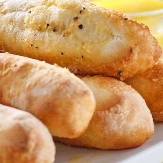 Drei goldbraune Brotstangen liegen auf einem weißen Teller. Jeder Stab hat eine knusprige Kruste und ist mit Kräutern bestreut. Die Brotstangen sind gerollt und bereit zum Verzehr.