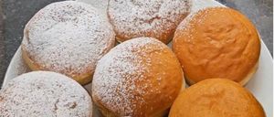 Ein Teller mit sechs Donuts, bestreut mit Puderzucker, steht auf einer dunklen Oberfläche. Drei der Donuts sind hellbraun, die anderen drei dunkler.