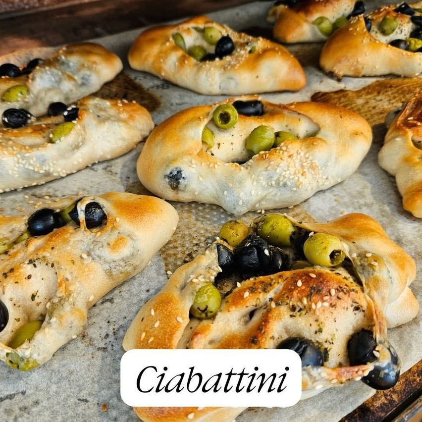 Ein Blech mit mehreren Ciabatta-Brotscheiben, gefüllt mit Oliven und mit Sesam bestreut, auf einem Backblech.