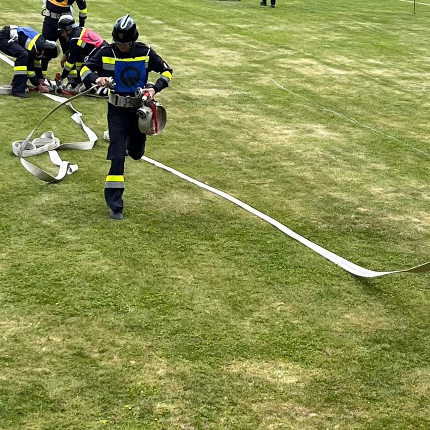 Feuerwehrleute üben auf einem Rasenfeld. Einer rennt, während andere sich um Ausrüstung kümmern. Einige tragen Helme und tragen Sauerstoffflaschen.