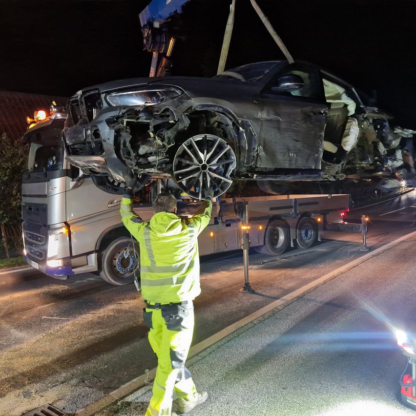 Ein Mann in Warnkleidung entfernt ein demoliertes Auto von einem Lkw bei Nacht.