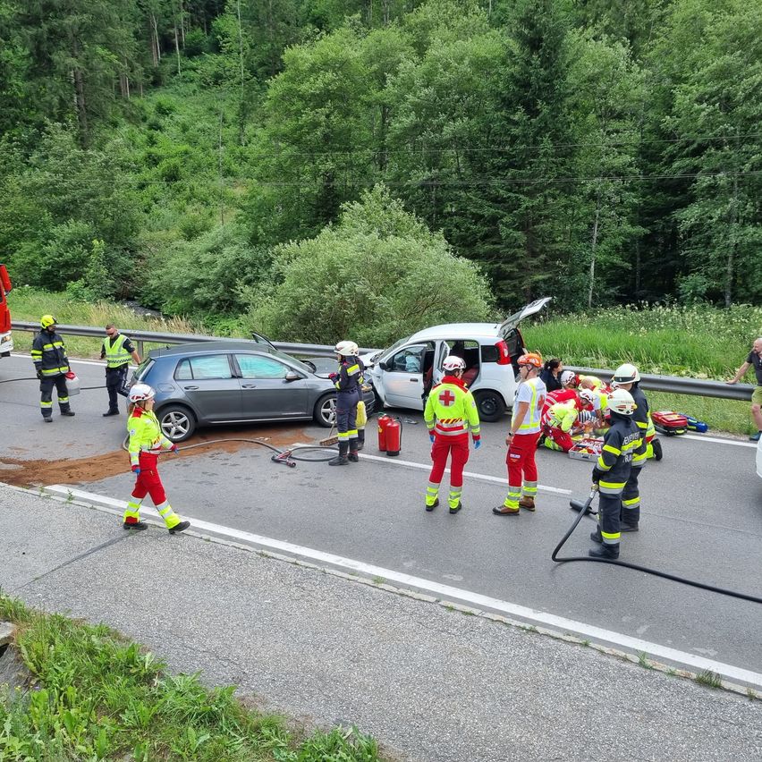 Emergency workers and bystanders assist the injured on a roadside. A fire truck and two cars are involved in the accident.