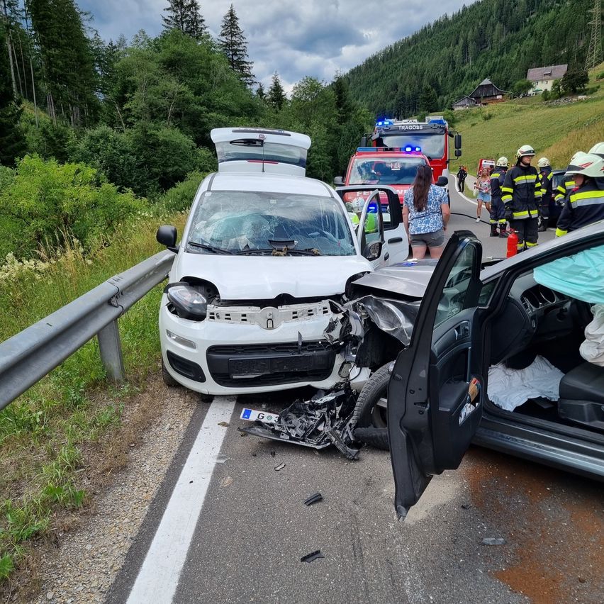 Two vehicles are wrecked on a rural road. Emergency services are attending to the scene. A fire truck and several firefighters are present.
