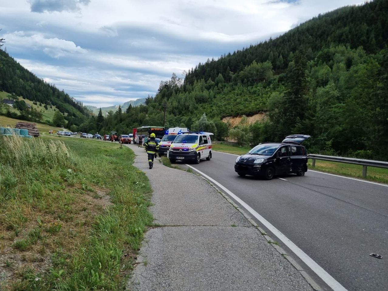 An accident on a road with emergency vehicles and a firefighter attending to the scene. A black car is stopped in the right lane.