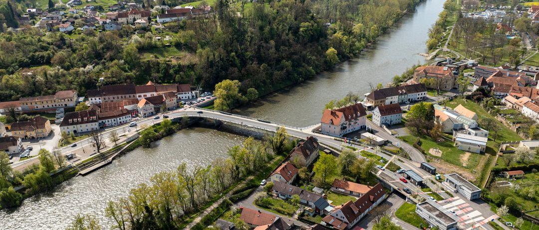 Eine Luftaufnahme einer kleinen Stadt am Fluss mit Häusern, Gebäuden und Bäumen in der Umgebung.