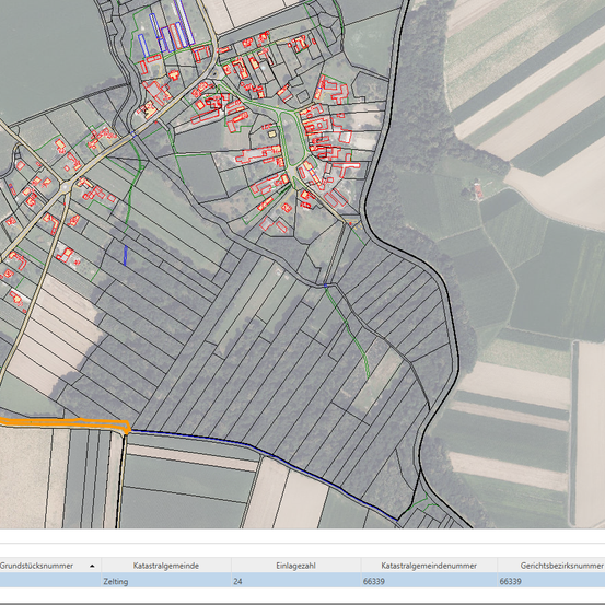 Eine Satellitenaufnahme eines ländlichen Gebiets mit einer Straße, Gebäuden und einem großen Feld. Die Gebäude sind rot und die Straße orange. Das Bild hat ein Rasterlayout.