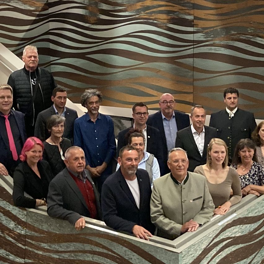 Eine Gruppe von Erwachsenen steht mit den Armen auf der Balustrade einer Treppe. Sie tragen alle formelle Kleidung.
