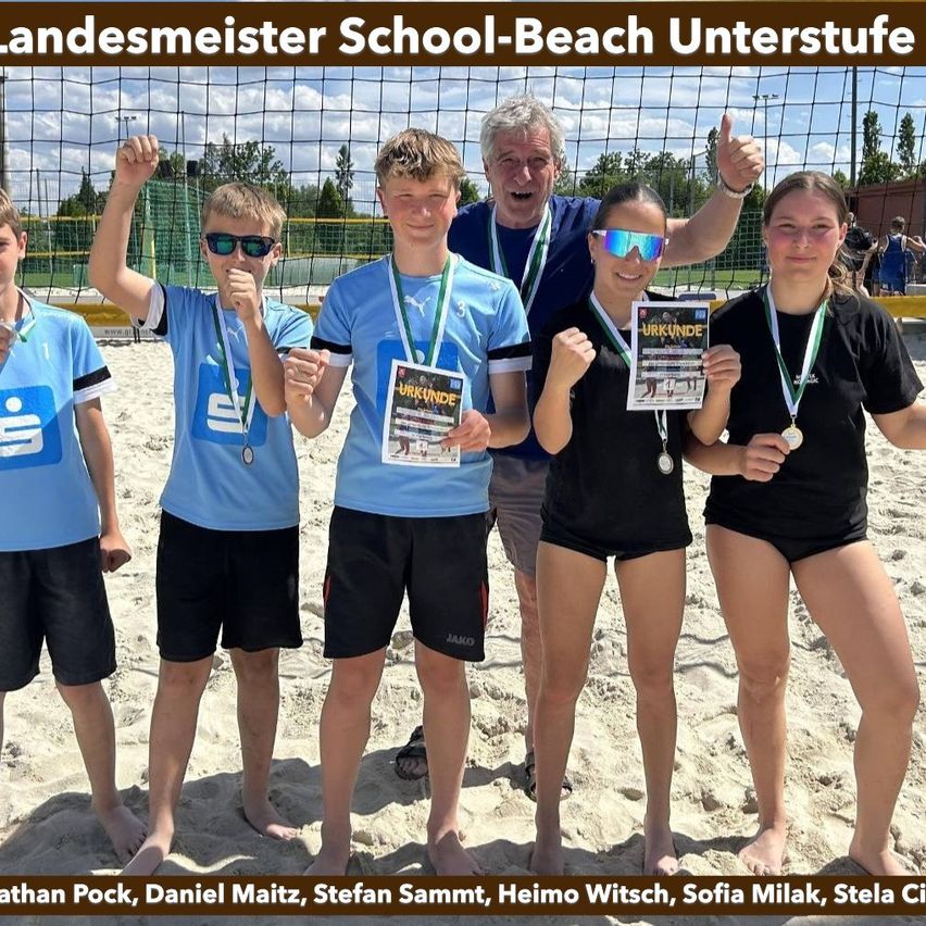 Eine Gruppe junger Athleten am Strand hält Medaillen. Sie tragen Trikots und Shorts und stehen vor einem Netz. Dahinter ist ein unscharfer Hintergrund eines Volleyballfeldes.