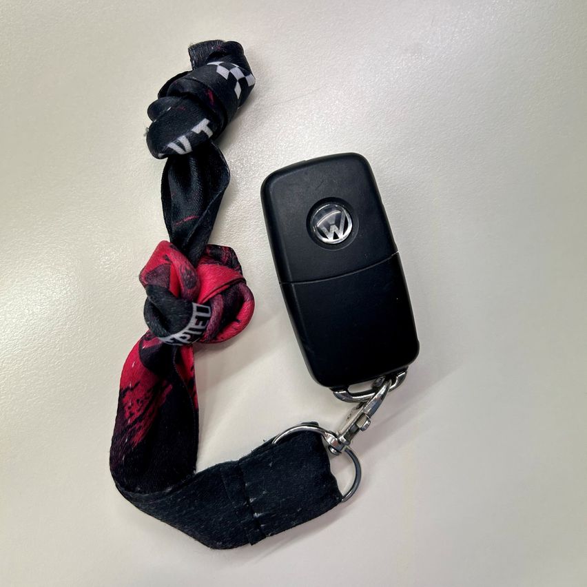 Ein schwarzer Volkswagen-Schlüssel mit einem Schlüsselanhänger mit einem Schal in Schwarz, Weiß und Rot liegt auf einer weißen Oberfläche.