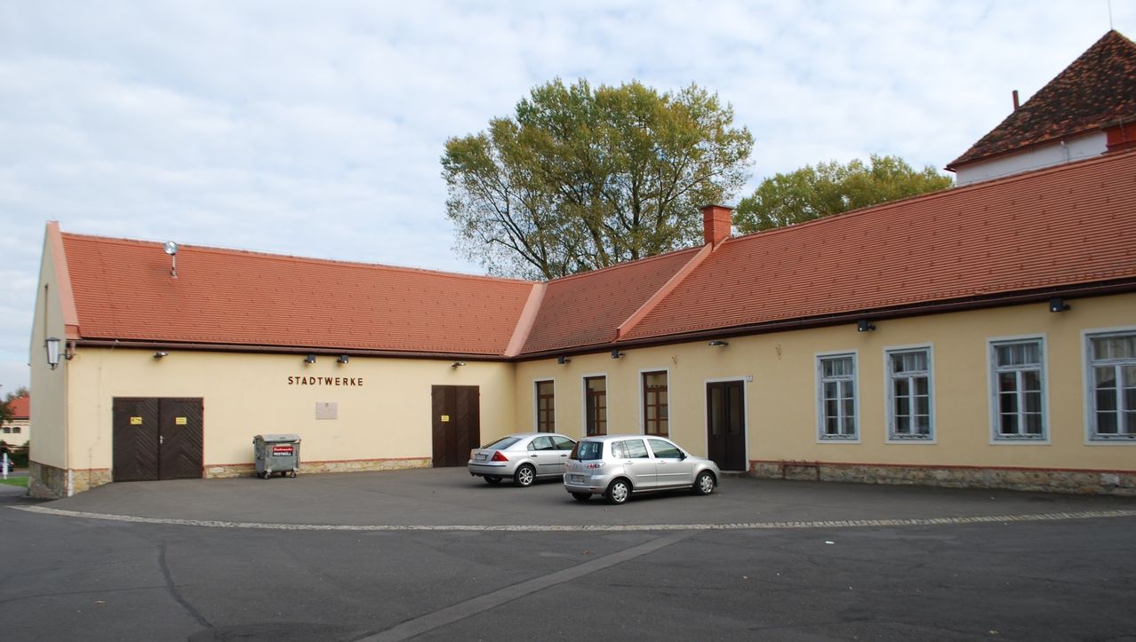 Ein Gebäude mit rotem Dach und der Aufschrift Stadtwerke. Zwei silberne Autos davor geparkt. Bäume stehen hinter dem Gebäude.