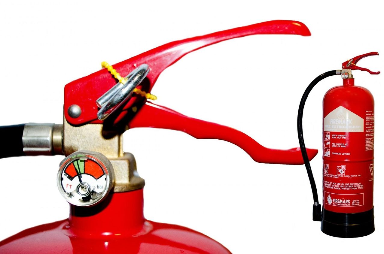 Ein Nahaufnahme eines roten Feuerlöschers mit einem schwarzen Schlauch und einem silbernen Messgerät auf weißem Hintergrund.