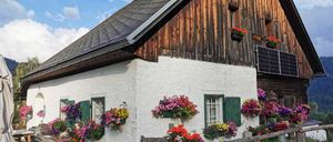 Ein charmantes rustikales Haus mit hölzerne Außenwand und weißer Basis, geschmückt mit bunten Blumen und einer Solaranlage auf dem Dach.