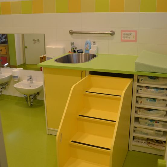 Ein Badezimmer mit gelben und grünen Akzenten, ausgestattet mit einem Waschbecken, einem Spiegel und einem Regal mit Aufbewahrungsboxen, sowie einer gelben Leiter.