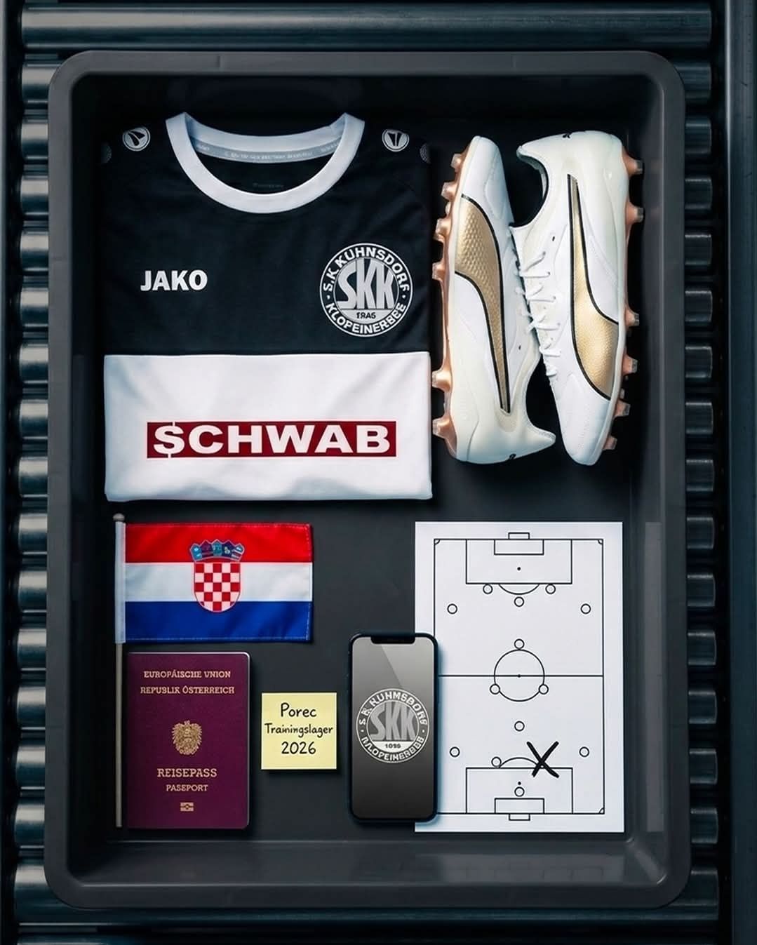 Eine Sport-Sammlervitrine enthält ein schwarzes Fußballtrikot mit dem Wort Jako, ein weißes Hemd mit Schwab und ein Paar weiße Fußballschuhe. Es enthält auch einen Reisepass, eine Flagge von Kroatien und ein Smartphone.