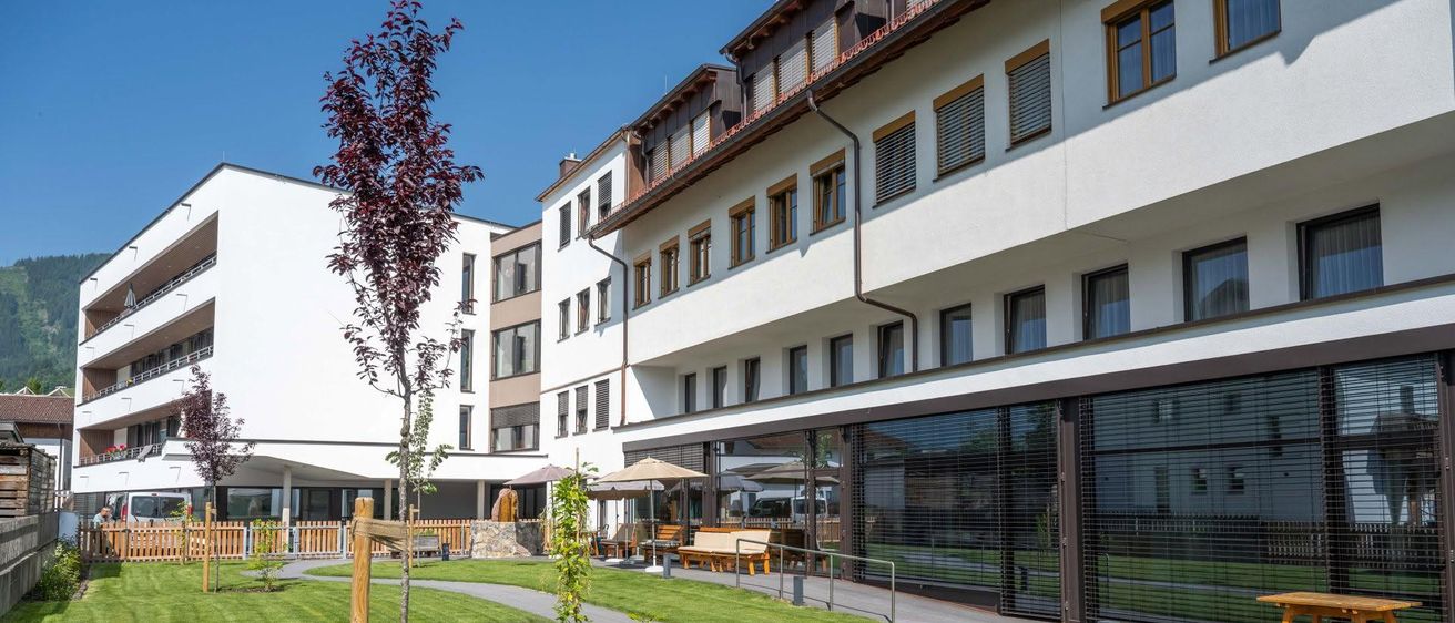 Ein modernes Apartmentgebäude mit einem gepflegten Rasen, einem Weg, Bänken und Sonnenschirmen.