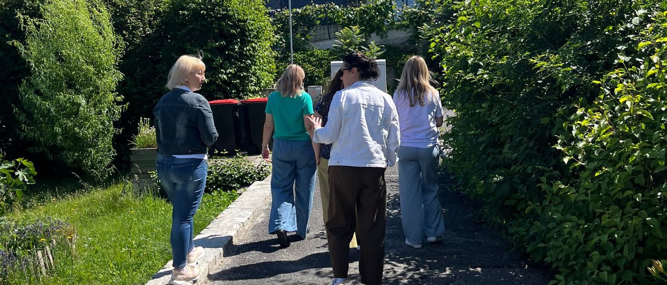 Eine Gruppe von Frauen geht auf einem von Grünpflanzen umgebenen Pfad. Das Wetter ist sonnig mit klarem blauem Himmel.