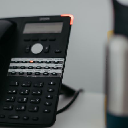 Nahaufnahme eines schwarzen Bürotelefons mit vielen Tasten und LED-Anzeigen. Die Nummer 1 ist rot markiert.
