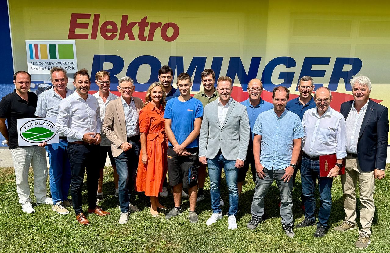 Eine Gruppe von Menschen steht vor einem Elektro Rominger-Banner und lächelt für ein Foto. Männer und Frauen in verschiedenen Outfits sind anwesend.