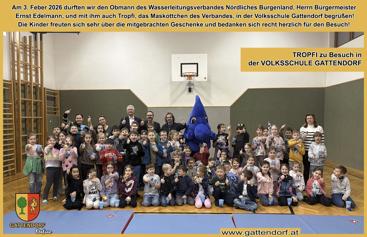 Eine große Gruppe von Kindern und Erwachsenen versammelt sich in einer Turnhalle. Sie halten Tassen und lächeln. Ein Maskottchen ist anwesend. Die Turnhalle hat einen Basketballkorb.