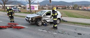 Ein zerkratztes silbernes Auto steht mit Trümmern am Straßenrand. Ein Feuerwehrmann steht daneben, und ein Polizeiauto ist in der Nähe.