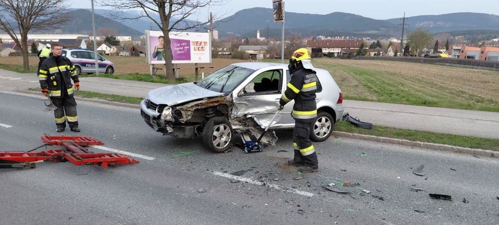 Ein zerkratztes silbernes Auto steht mit Trümmern am Straßenrand. Ein Feuerwehrmann steht daneben, und ein Polizeiauto ist in der Nähe.