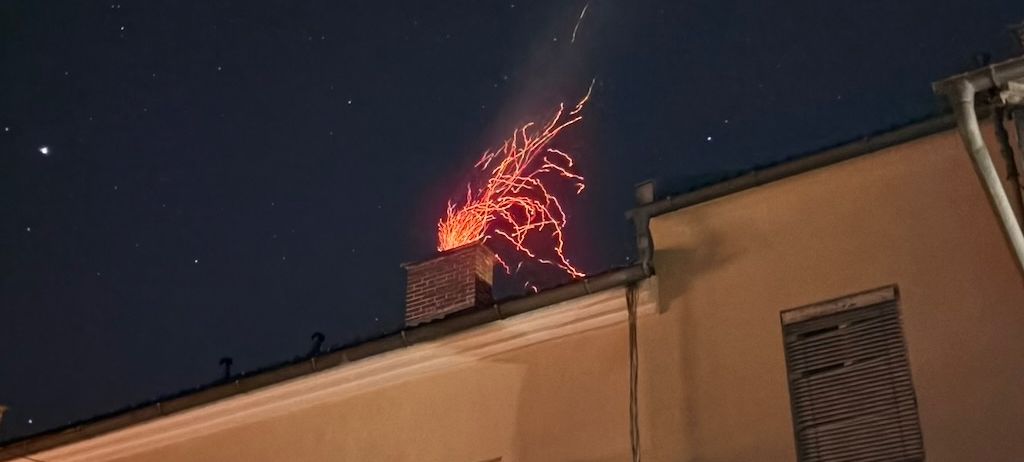 Ein Gebäude mit einem Feuer auf dem Schornstein. Es ist Nacht und der Himmel ist dunkel. Das Gebäude hat Fenster und eine Satellitenschüssel.