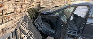 Ein schwarzes Auto ist am Straßenrand geparkt, der vordere Stoßfänger beschädigt, mit geöffneter Fahrertür.