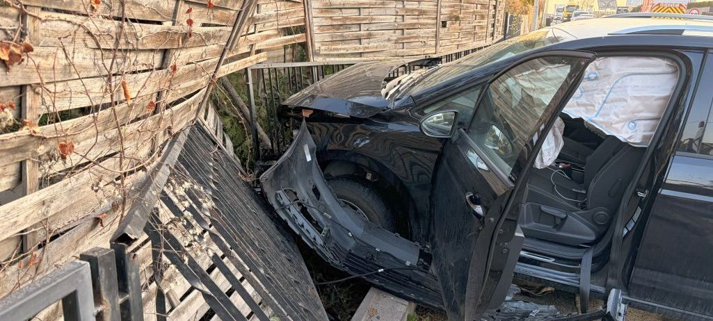 Ein schwarzes Auto ist am Straßenrand geparkt, der vordere Stoßfänger beschädigt, mit geöffneter Fahrertür.