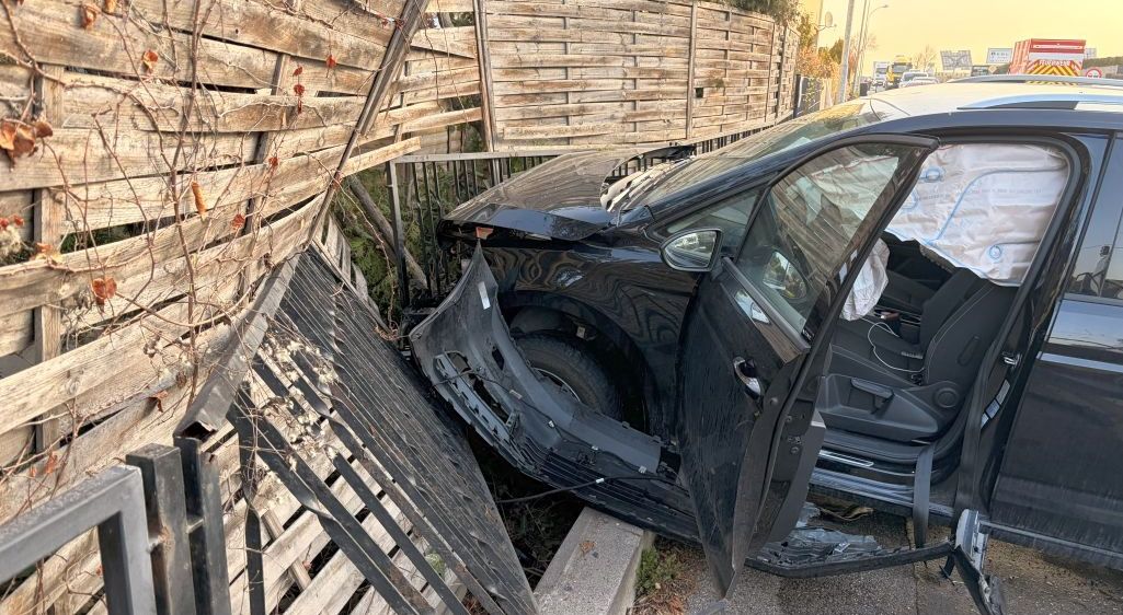 Ein schwarzes Auto ist am Straßenrand geparkt, der vordere Stoßfänger beschädigt, mit geöffneter Fahrertür.