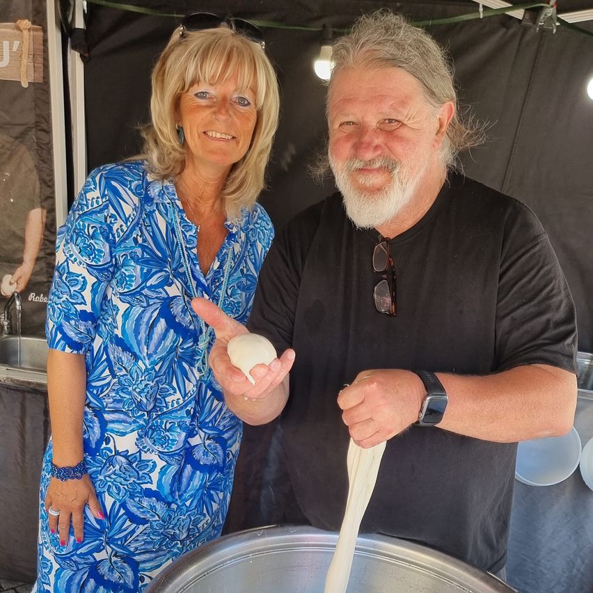 Ein Mann und eine Frau stehen in einer Küche, er zieht Teig aus einem Topf. Sie lächeln und stehen in der Nähe einer Spüle.