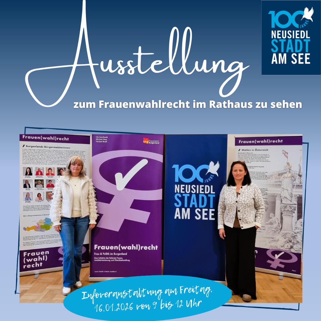 Zwei Frauen stehen neben Bannern, eines mit lila Hintergrund und eines mit blauem Hintergrund. Das blaue Banner trägt die Aufschrift '100 Jahre Neusiedl am See.' Sie befinden sich auf einer Ausstellung zum Frauenwahlrecht.