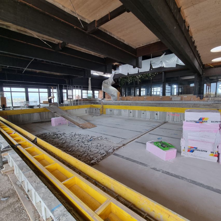 Ein Innenbaustelle mit großen Säulen und gelben Barrieren. Der Boden ist mit Kies gefüllt und hat eine pinke Box in der Nähe.