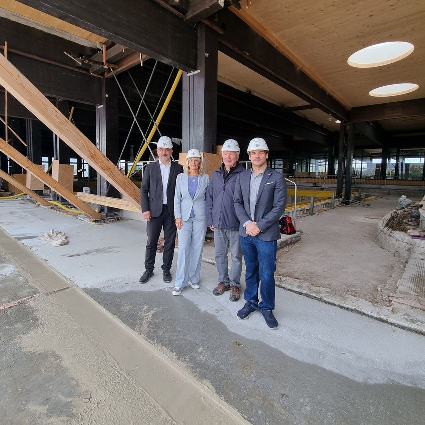 Vier Personen in Schutzhelmen stehen in einem im Bau befindlichen Gebäude und posieren für ein Foto.
