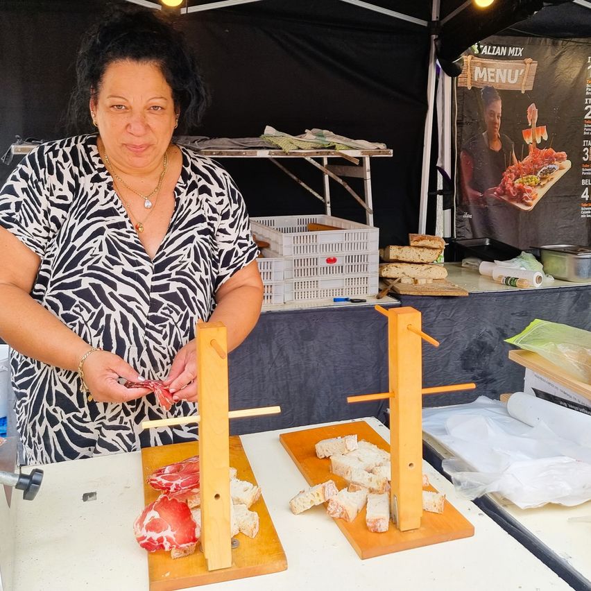 Eine Frau in einem Zebra-Print-Shirt schneidet Fleisch auf einem Holzbrett an einem Imbissstand.