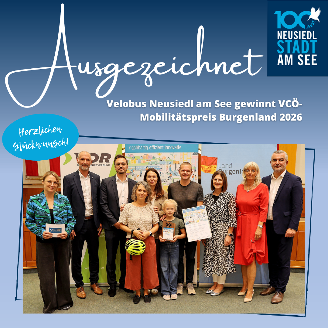 A group of people stands together holding awards and certificates, with a banner behind them that reads 'Velobus Neusiedl am See wins VCÖ Mobility Prize Burgenland 2026'. The image is set against a blue background.