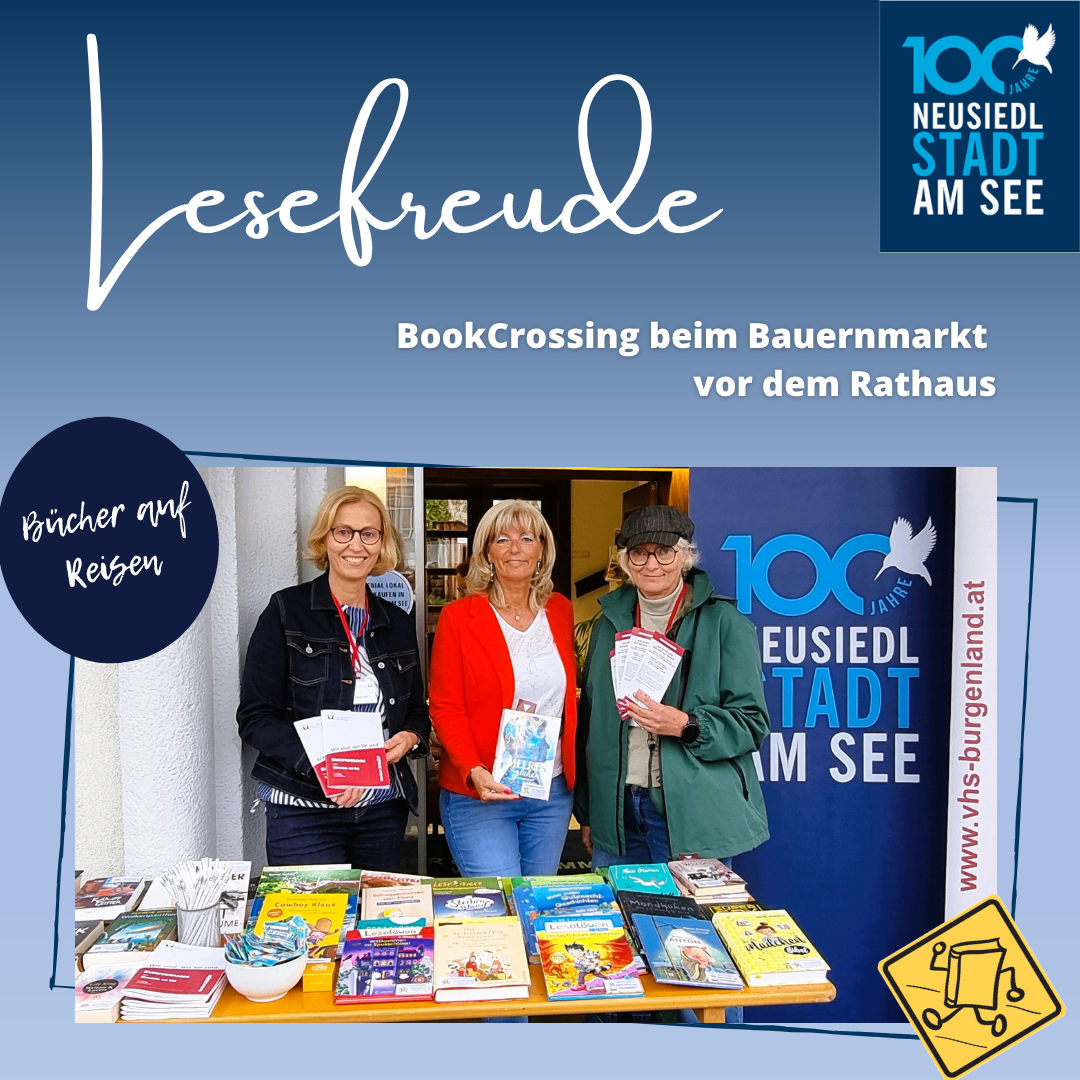 Three women stand behind a table of books, smiling for a photo. They are at a BookCrossing event at the farmers' market in front of the town hall.