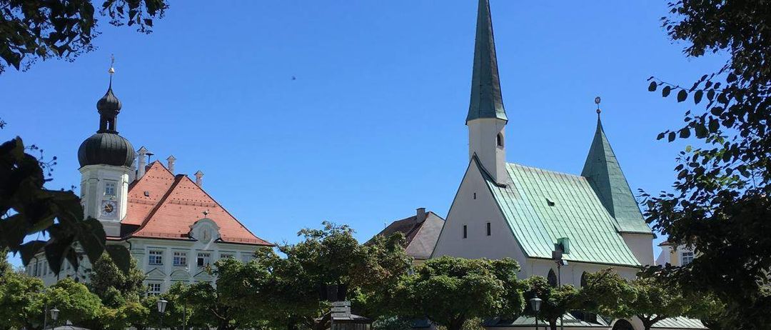 Eine große weiße Kirche mit grünem Dach und Turm steht in einem Park. Ein Uhr befindet sich auf dem Turm. Bäume umgeben das Gebiet, und eine Straße führt zum Gebäude.