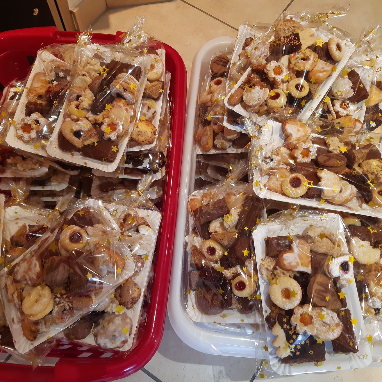 Zwei Tabletts gefüllt mit verschiedenen Arten von Keksen, jeder einzeln in Plastik verpackt. Die Kekse sind mit Sternen verziert und kommen in verschiedenen Formen und Geschmacksrichtungen.
