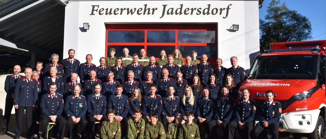 Eine Gruppe von Feuerwehrleuten der Feuerwehr Jadersdorf posiert vor ihrem Feuerwehrhaus.