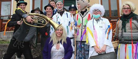 Eine Gruppe von Menschen in verschiedenen Kostümen posiert für ein Foto vor einem Gebäude. Das Schild darüber lautet Gasthof Purrer. Die Kostüme umfassen einen Clown, einen Arzt und andere.