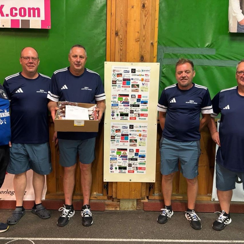 Fünf Männer stehen nebeneinander und tragen blaue Uniformen. Ein Mann hält eine Schachtel mit Essen, und hinter ihnen ist ein Poster mit vielen Aufklebern.